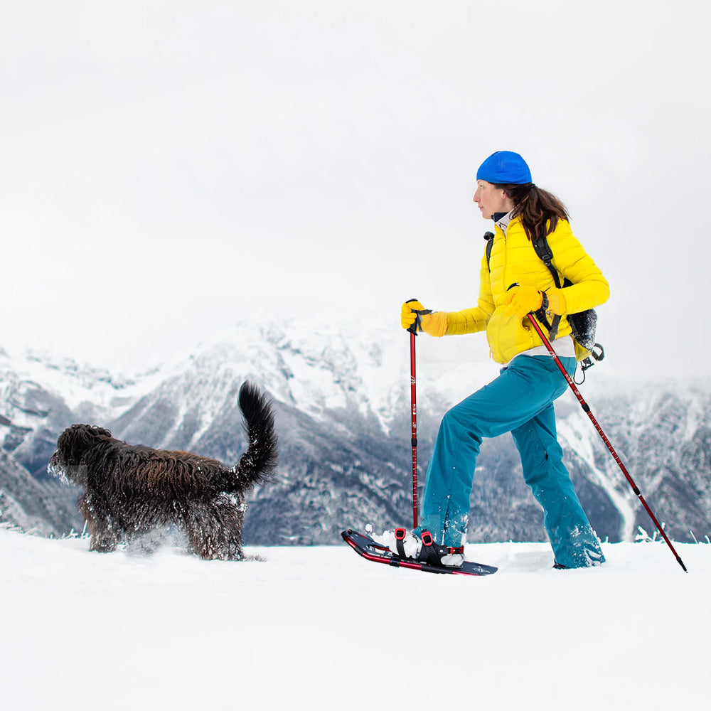 A woman walks in the snow with her dog wearing women's snowshoes